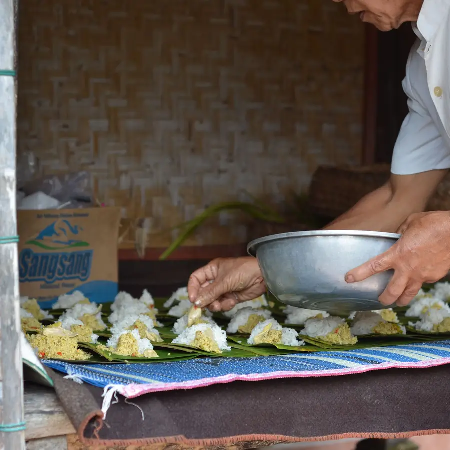 Hands preparing rice parcels wrapped in banana leaves