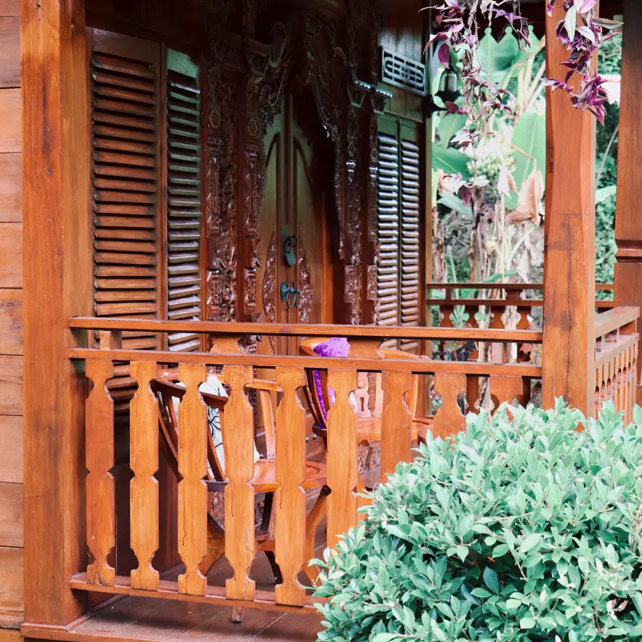 A carved wooden porch framed by green plants