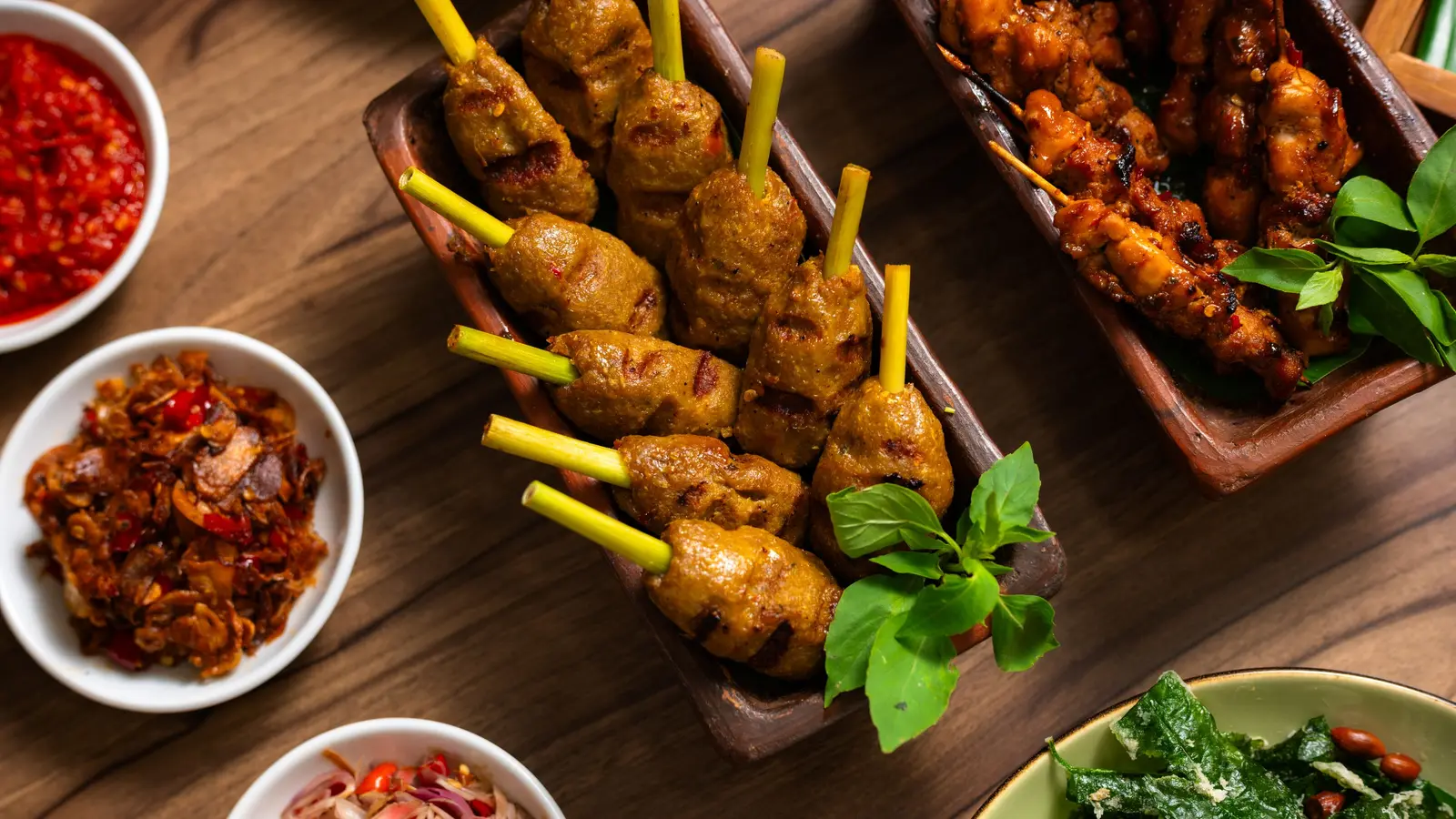 Satay, sambal and side dishes on a wooden table