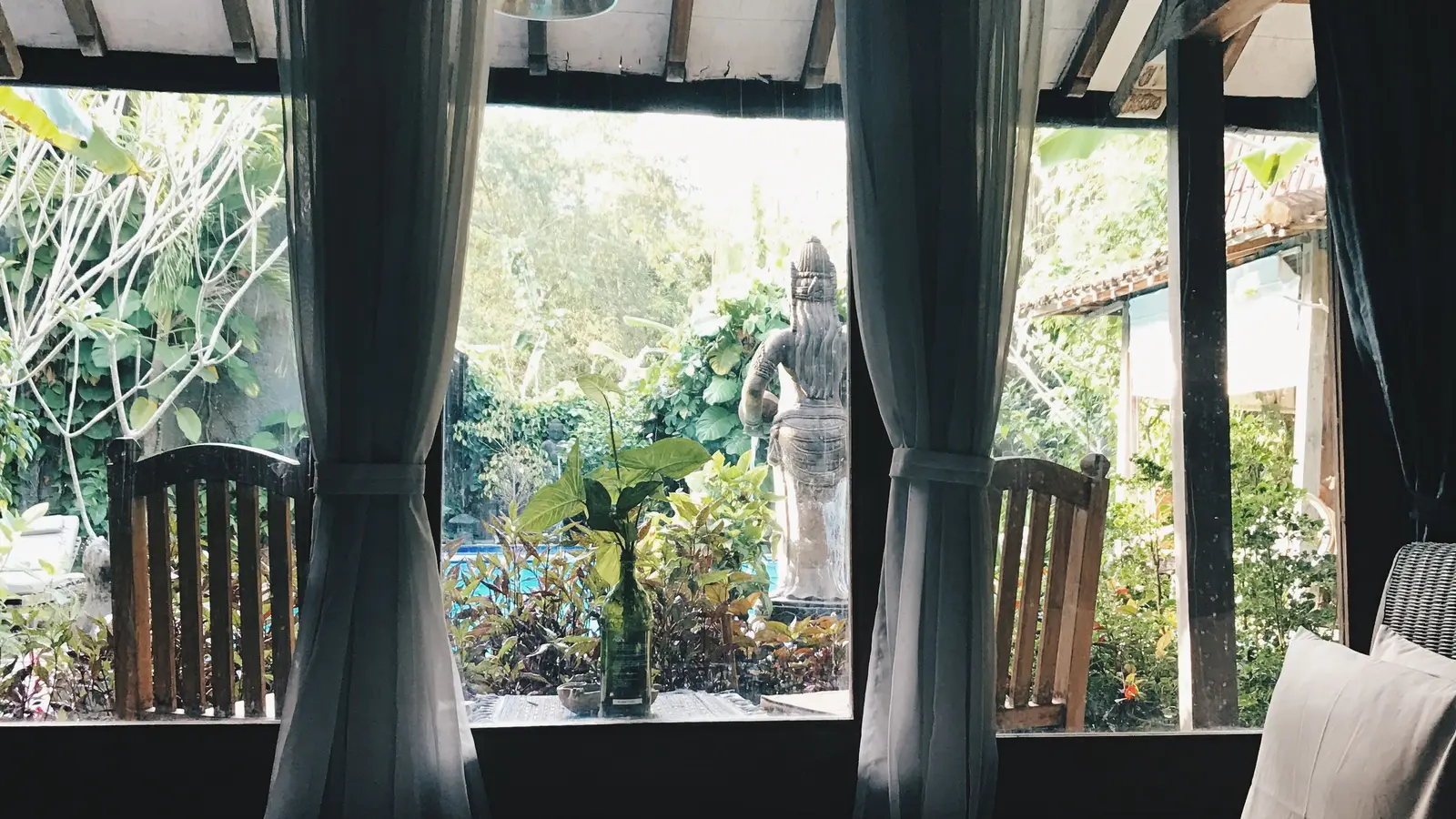 A bedroom with a large window looking onto a green garden